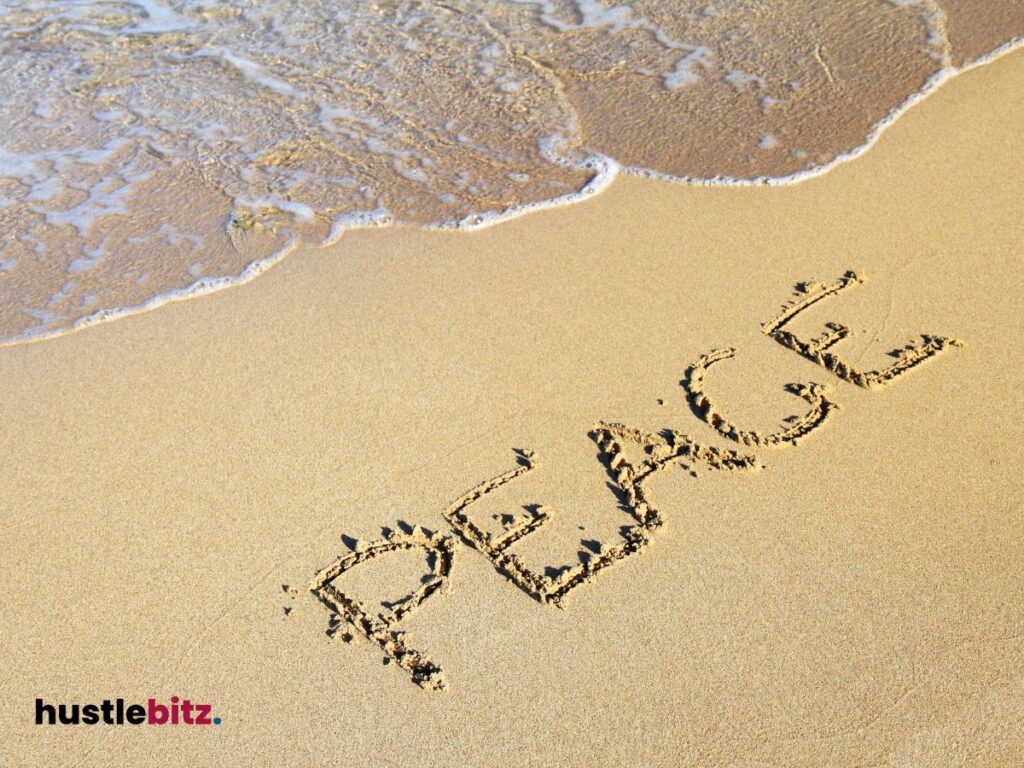 The word "PEACE" is written in sand, gently touched by calming ocean waves.