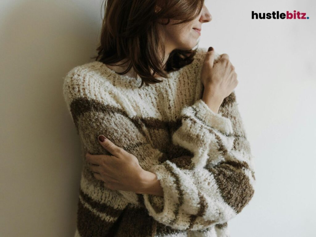 A woman in a cozy sweater hugs herself, showing self-love and warmth.