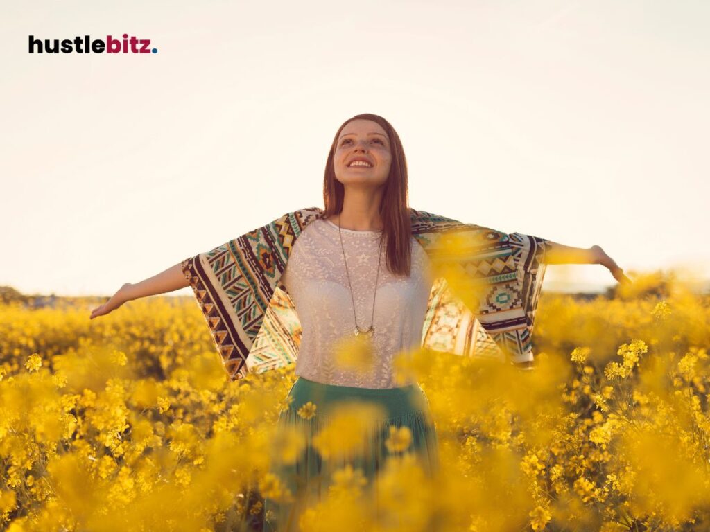 A woman smiles, arms open, standing in a vibrant yellow flower field.