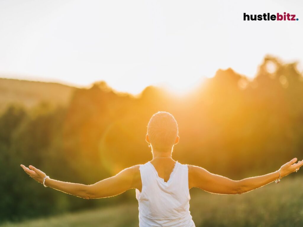 A person stands with open arms, embracing the warm glow of a golden sunrise.