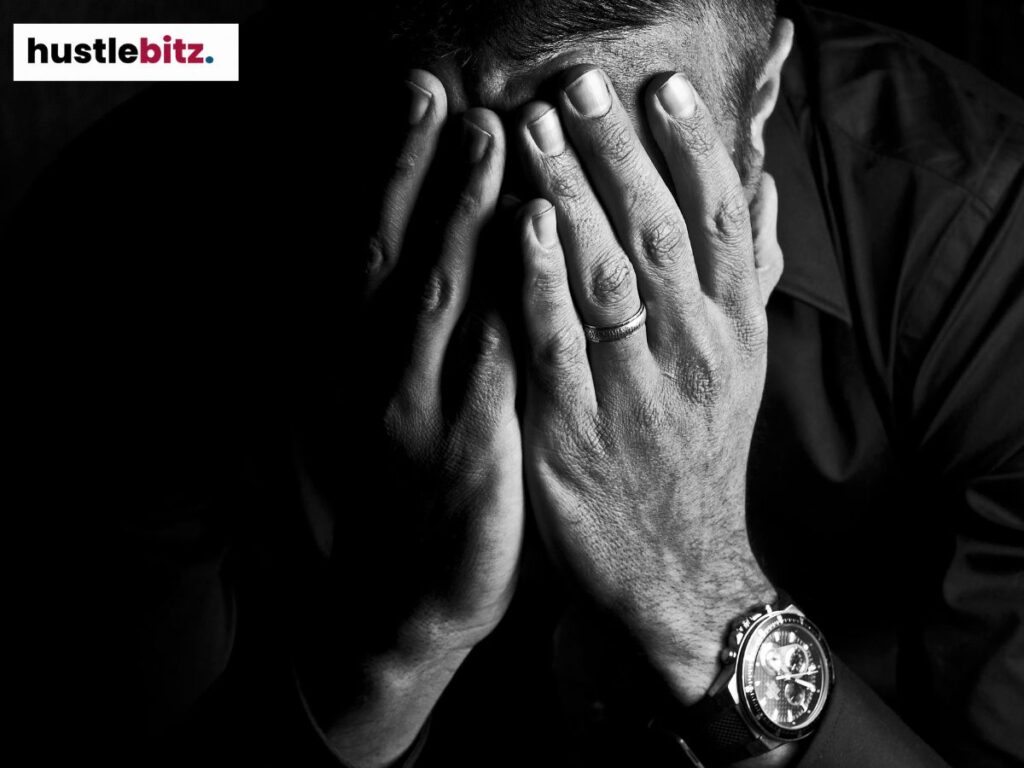 A man covers his face with both hands, expressing deep stress or sadness.