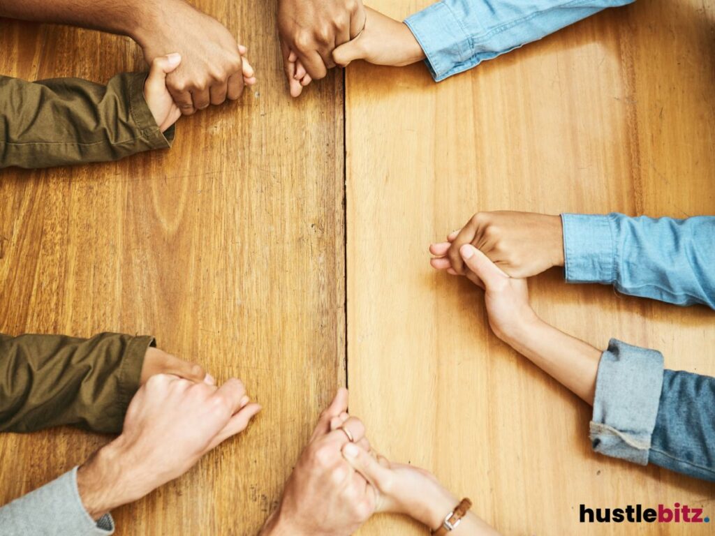 Multiple hands holding each other around a wooden table, symbolizing unity and support.