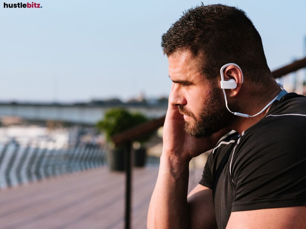 Man outdoors wearing earphones, looking thoughtful.