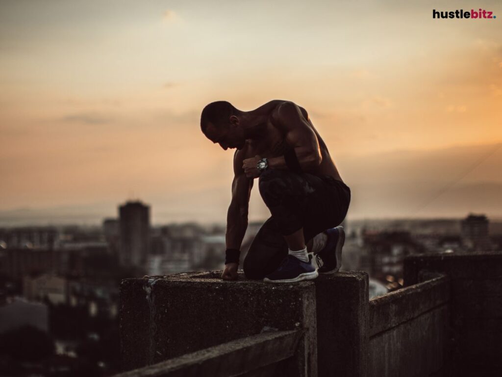 Man crouching on a ledge at sunset .