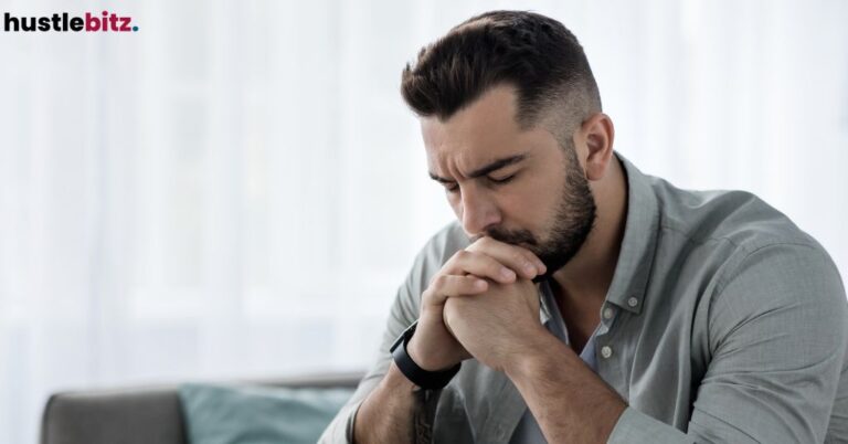 A man sitting on a couch closing his eyes na putting his hands together.