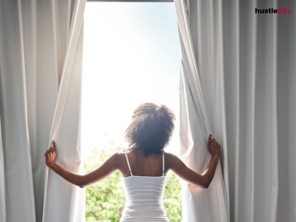 Woman opening white curtains, looking outside.