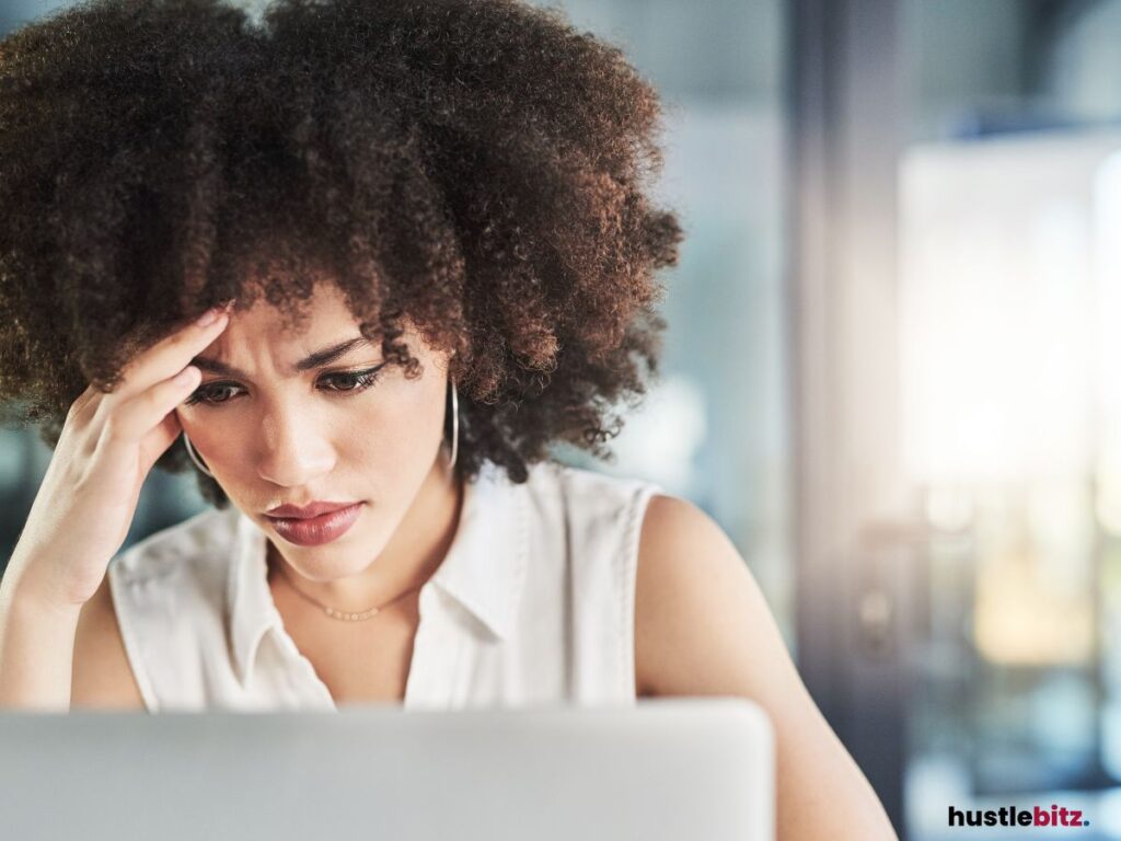 Woman frowning at a laptop, hand on forehead.