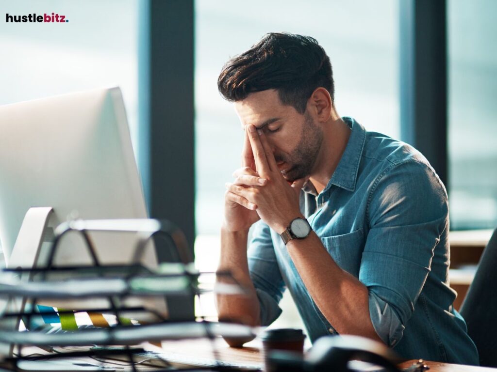 Man at a desk, stressed, rubbing his eyes.