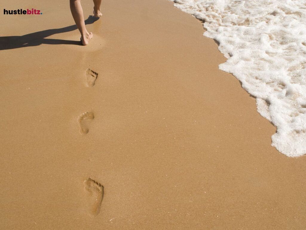 Barefoot person walking on a beach, leaving footprints.
