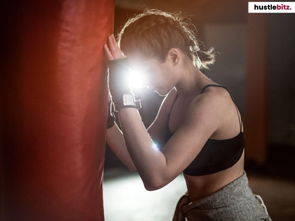 A woman doing boxing, holding the paunching bag.
