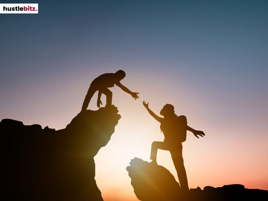 Two person climbing a mountain with one person extending her hand.