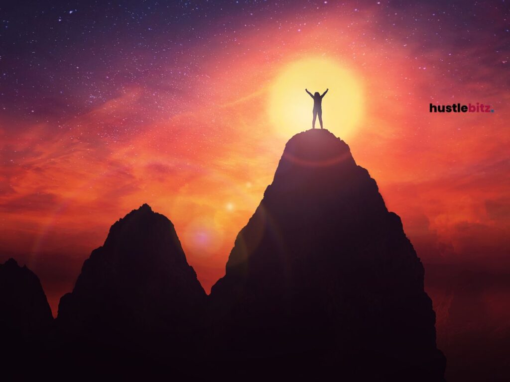 A silhouette of a person standing in the peak of a mountain.
