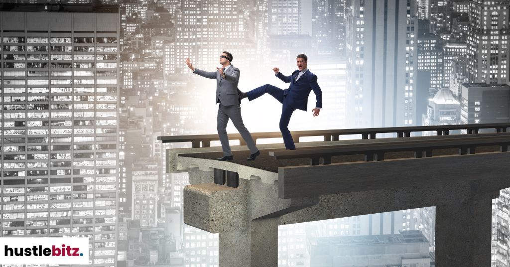 A man kicking a blindfolded man in the end of the bridge.