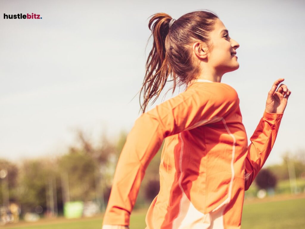 A woman running outdoors on a sunny day, wearing an orange athletic top.