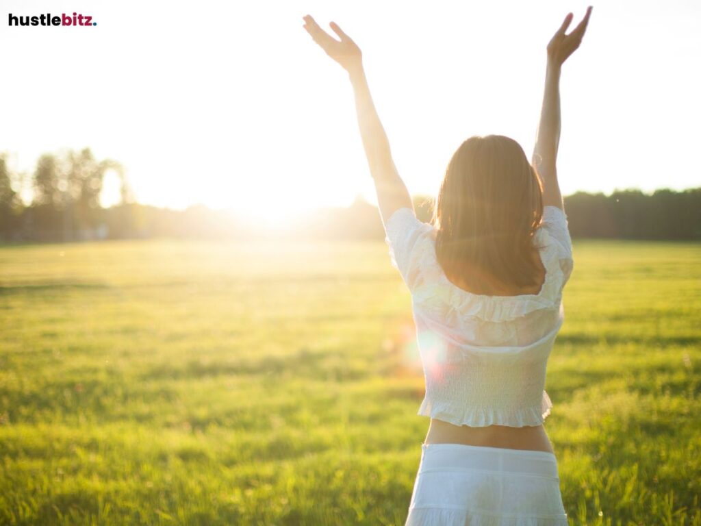 A woman standing in a field, arms raised toward the bright sun, embracing the moment.