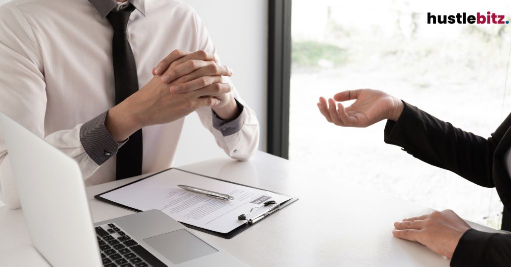 Business conversation at a desk with a clipboard and a laptop on the table.